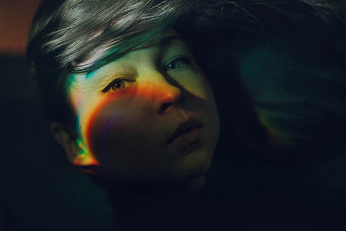 Mysterious self portrait photography showing rainbow effect on a girls face created with a CD